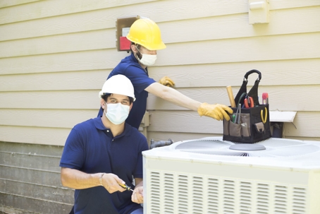 Two HVAC technicians working on a residentail central air conditioning condenser