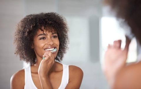 Woman brushing her teeth while looking in the mirror